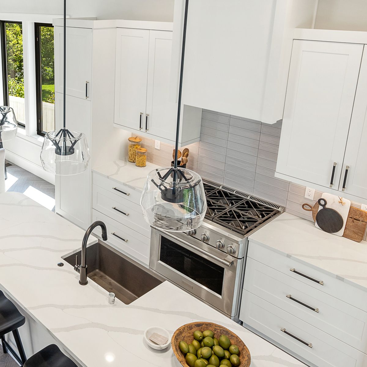 Modern kitchen with white cabinets and drawers, silver appliances, ranch style sink, white tile backsplash and white marble countertops. 
