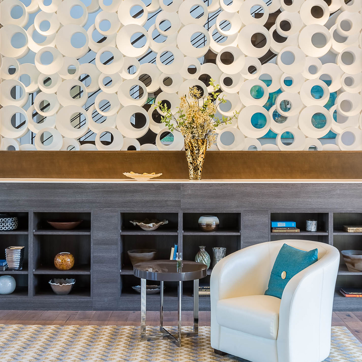 Modern waiting area with white leather chair, metal side table with open faced dark wood shelving. Pottery is sitting in the spaces in the shelving. 